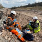 Two employees in high-visibility clothing sitting on a worked earth track.